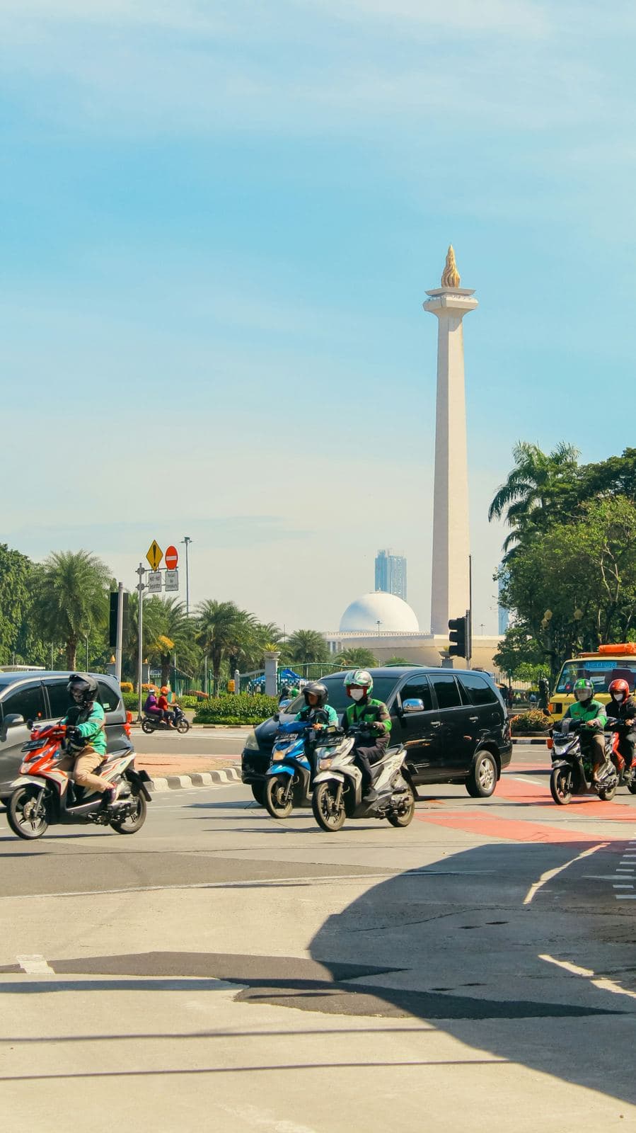 Lalu lintas sepeda motor di jalan Jakarta dengan Monas di kejauhan
